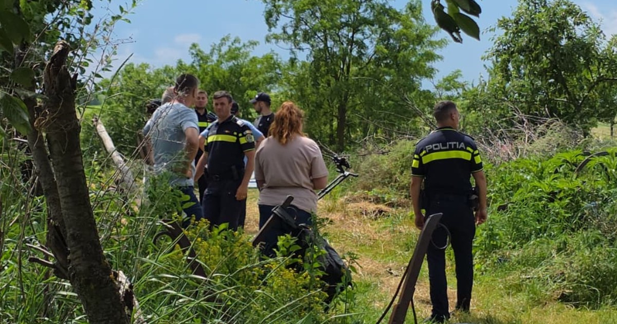 Imaginea prezintă un grup de polițiști români și civili adunați într-o zonă rurală cu verdeață și vegetație deasă în cadrul unei anchete.