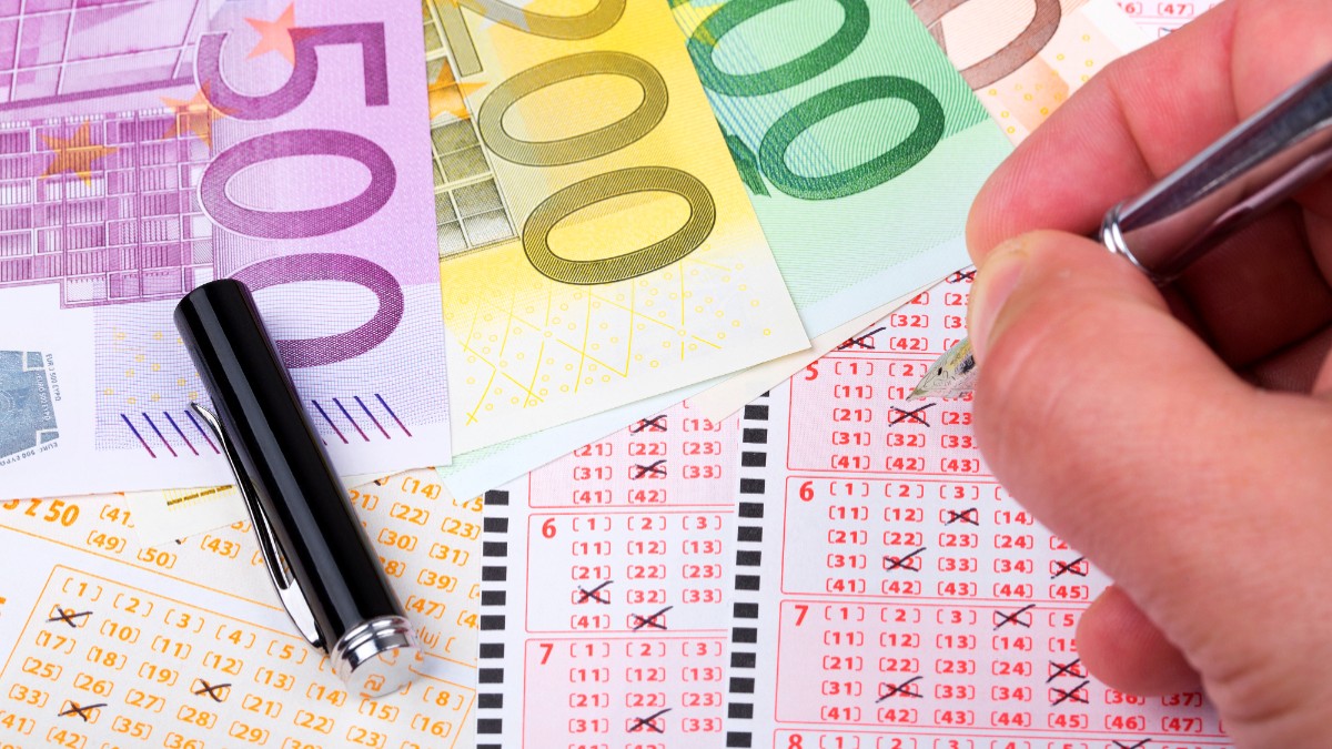 Bancnote euro pe un bilet la loto. Un bărbat ține un pix în mână.