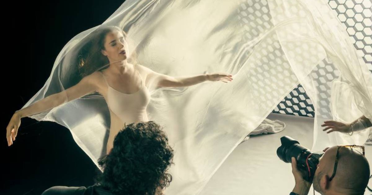 Un model, peste care pluteste o panza alba, transparenta, intr-un studio foto, cu doi fotografi in fata, in timpul sedintei pentru Calendarul Pirelli 2026
