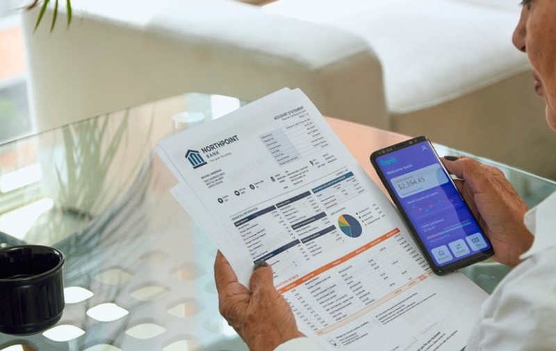 A senior woman pays her utility bills through the banking app on her phone.