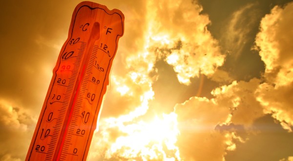 Un termometru ce indică o valoare ridicată de aproximativ 36 de grade Celsius, profilat pe un cer luminos de vară cu raze puternice de soare care creează un efect cald, portocaliu-auriu
