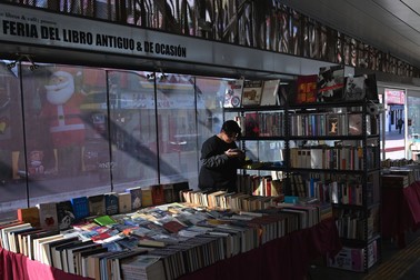 Axel Gonzalez, a book reseller and exhibitor from Mexico City, takes a break by reading one of his books at the Occasional Used Book Store "Antiguo" Fair at a downtown Revolution Avenue bus station of the Tijuana Comprehensive Transportation System (STT) in Tijuana, Mexico on Monday, December 16, 2024. Rene Castillo from the Graphographer: books &amp; coffee shop and organizer of the book fair highlighted that the fair was taking and intervening in public spaces like the not so used bus station, to bring books closer to people and ferment a culture of book reading and appreciation, which was contemplated in collaboration with the local Tijuana government and the Municipal Institute of Art and Culture. Used Book Fair takes Tijuana, Mexico bus station, Baja California - 16 Dec 2024,Image: 947836603, License: Rights-managed, Restrictions: , Model Release: no