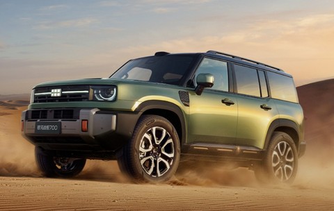 Un SUV off-road, de culoare verde măsliniu, rulând prin dunele de nisip ale unui deșert la apus.