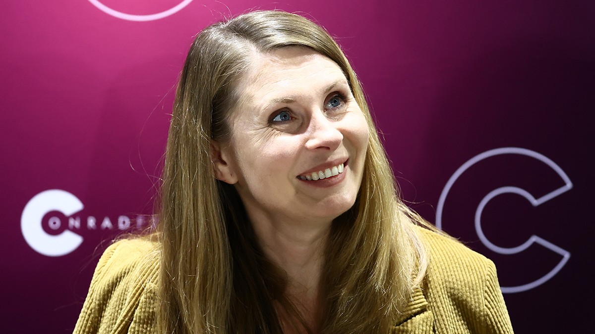 Tatiana Țîbuleac îmbrăcată într-o haină culoarea muștar și preveștîn sus, zâmbind.