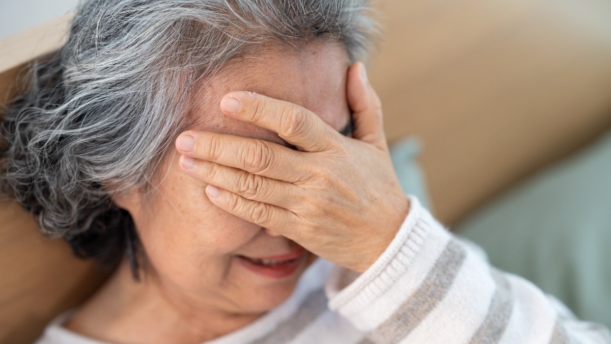 O pensionară care își ține mână la frunte și este supărată