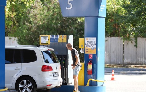 Un bărbat care se uită la ecranul unei pompe dintr-o stație de carburanți, lângă un autoturism alb Volkswagen parcat pentru alimentare.