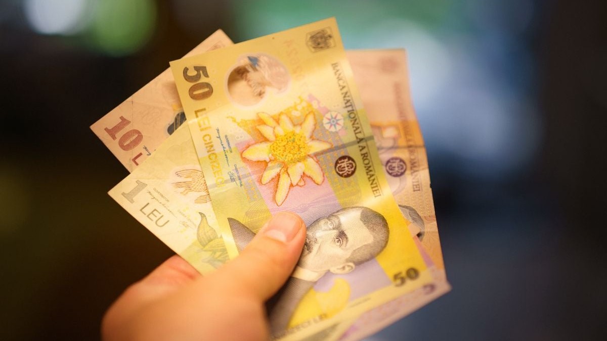 Bani, bancnote de 50 și 10 lei, ținuți în mână, cu o lumină caldă care bate spre ei