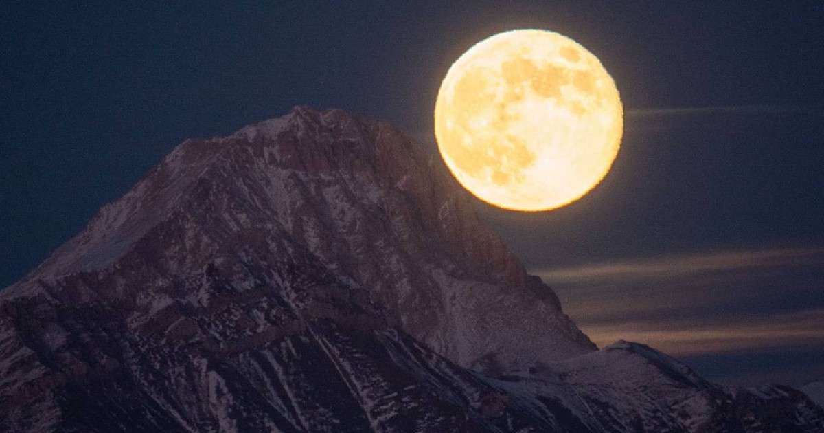Superluna se vede în spatele unui munte, strălucitoare și uriașă