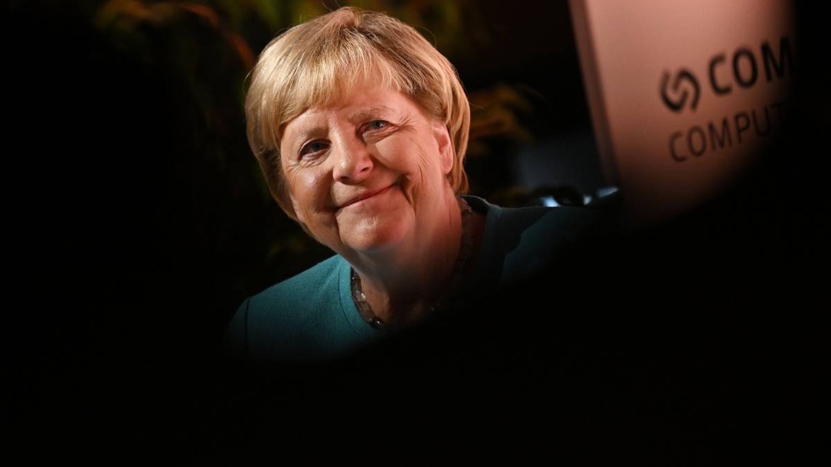 Fostul cancelar al Germaniei, Angela Merkel, îmbrăcată cu un sacou albastru, la un eveniment diplomatic. Are părul blond tuns scurt și zâmbește în fața camerei