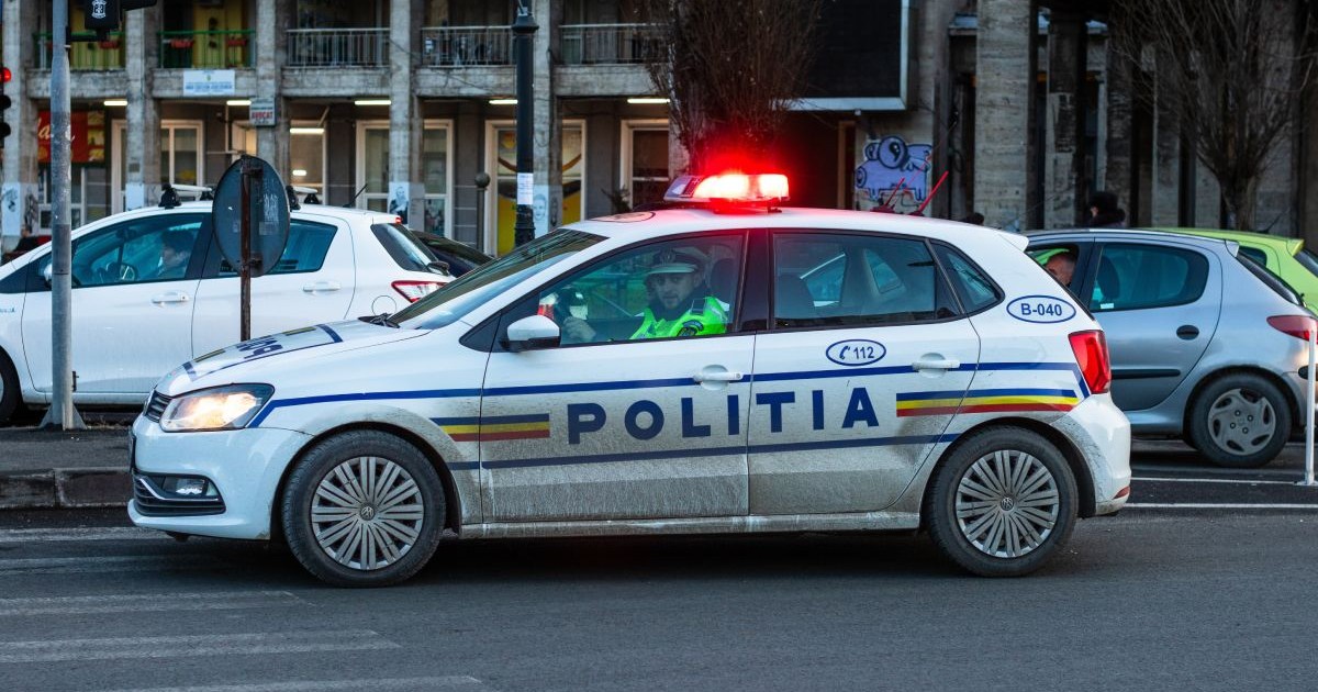 Mașină de Poliție, cu girofarul pornit, pe o stradă din București, cu doi polițiști îmbrăcați în uniforme în interior
