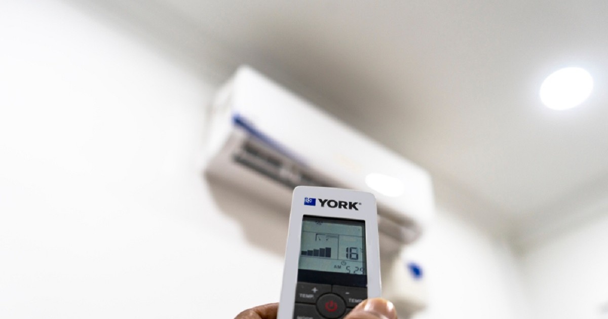 De ce nu trebuie să setezi aerul condiţionat la 16°C - Imagine cu mâna unui bărbat în care se află o telecomandă îndreptată către unitatea internă a aerului condiţionat