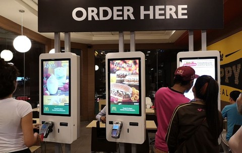 Oameni care stau la coadă la aparatul de comandă automată de la McDonald's