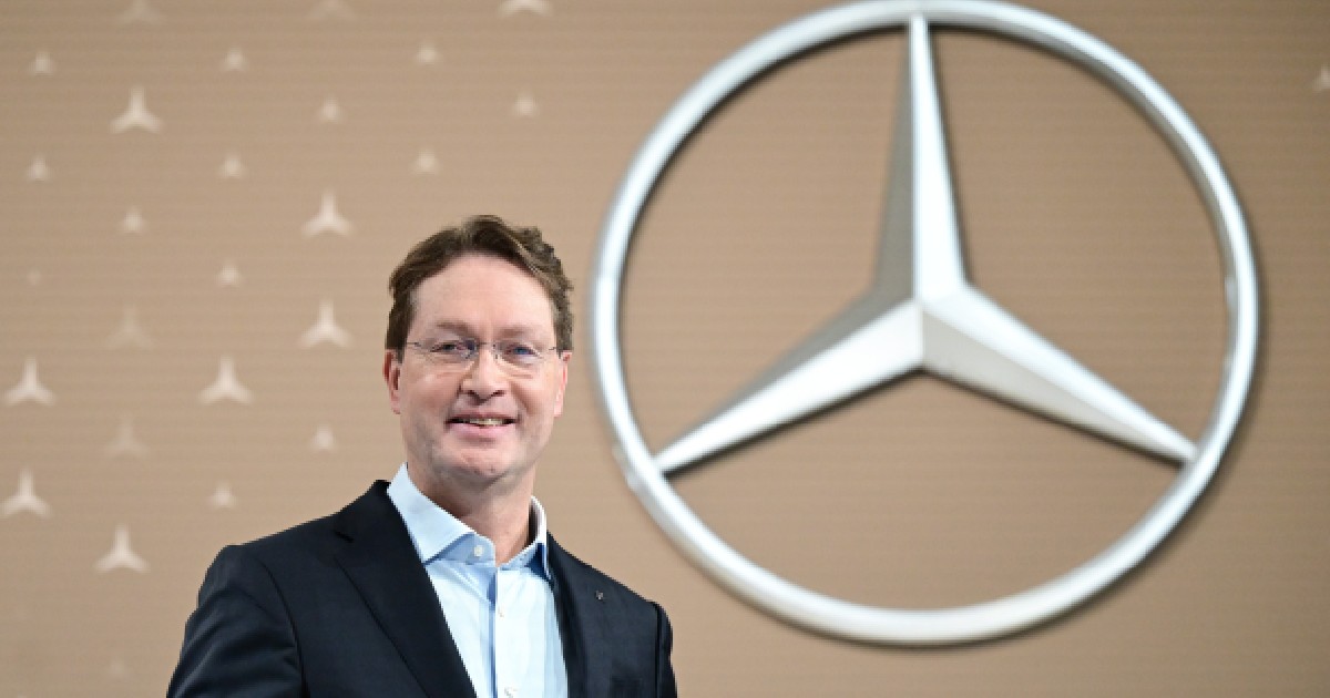 Ola Källenius în costum, zâmbind, cu sigla Mercedes în fundal