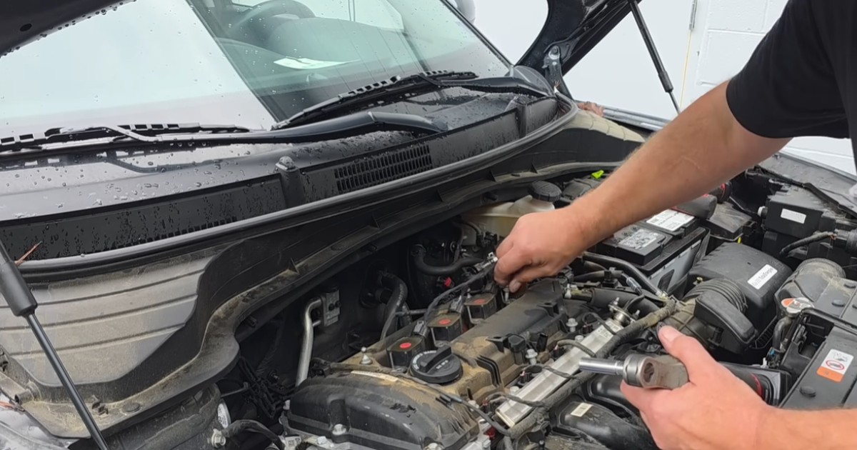 Un bărbat cu tricou negru care lucrează la compartimentul motor al unei mașini