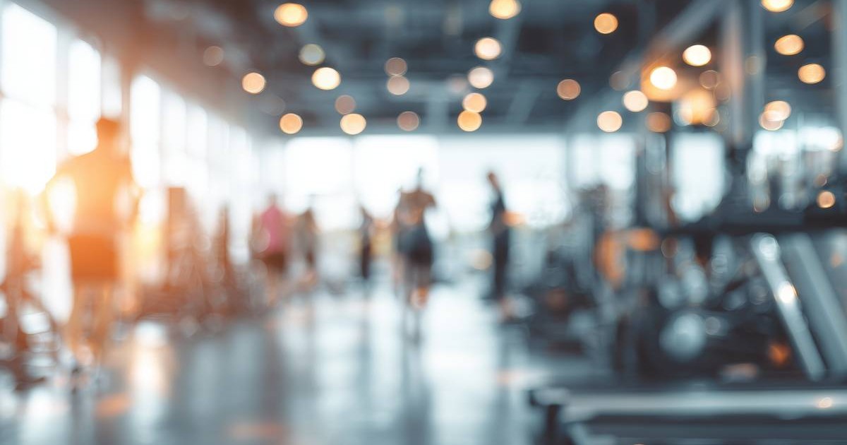 Imagine neclară a interiorului unei săli de sport aglomerate, se pot distinge oameni si benzi de alergare