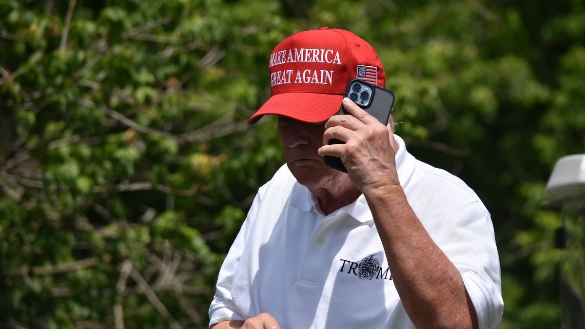 Donald Trump, în tricou alb și cu șapcă neagră, vorbește la telefon