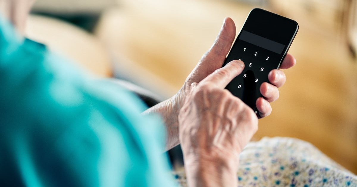 O femeie în vârstă în timp ce ține un telefon în mână și tastează un număr de telefon