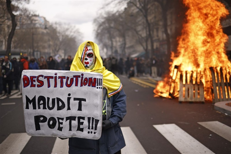 epa10538840 A protester holds a placard reading 'destitution cursed poet' in front of a fire as thousands of people participate in a protest against the government's reform of the pension system in Paris, France, 23 March 2023. Protests continue in France after the prime minister announced on 16 March 2023 the use of Article 49 paragraph 3 (49.3) of the French Constitution to have the text on the controversial pension reform law - raising retirement age from 62 to 64 - be definitively adopted without a vote. EPA-EFE/YOAN VALAT