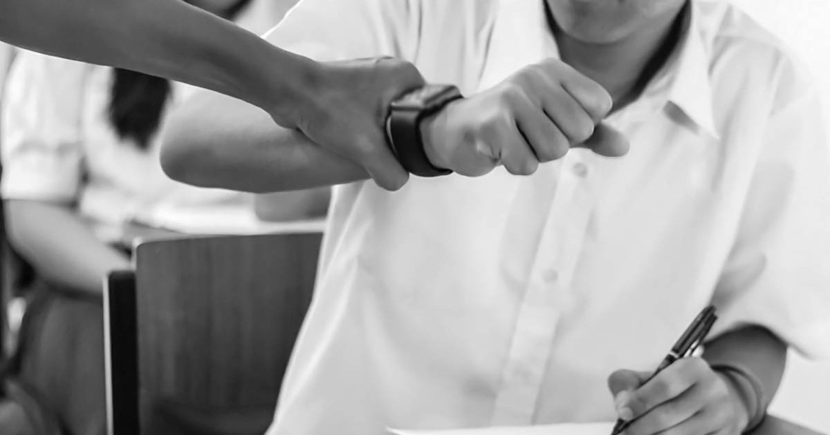 Cdru strans, amb negru, cu mana unei femei care strange mana unui elev cu un smart watch , in clasa, in timpul unui examen. Conceptul de abuz la scoala