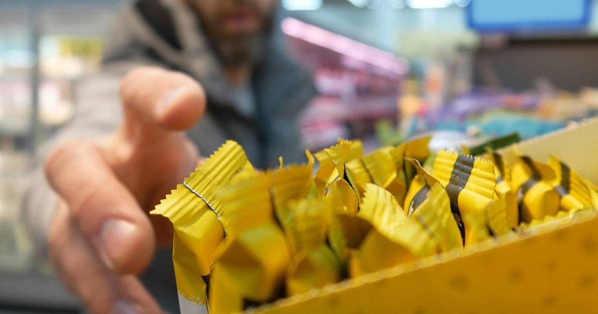 Prim-plan cu numeroase batoane pe raftul unui supermarket și un barbat care întinde mâna să ia una