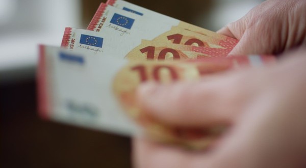 o mână care ține câteva bancnote de 10 euro, roșii și galbene