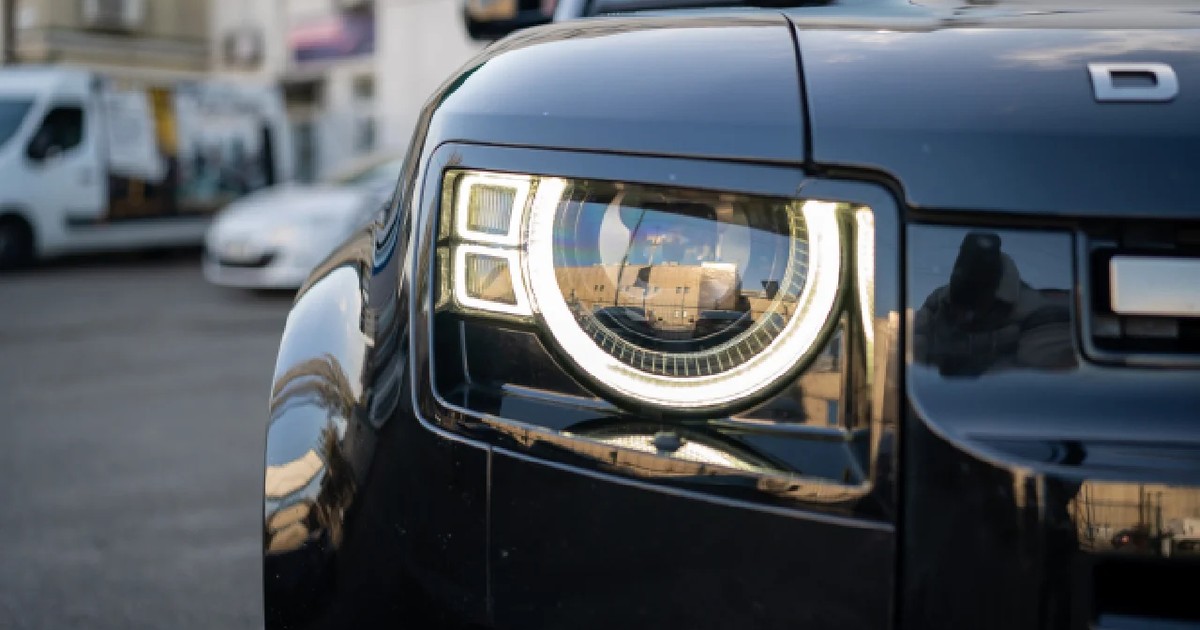 Plan apropiat cu un far aprins al unui Land Rover Defender de culoare neagră