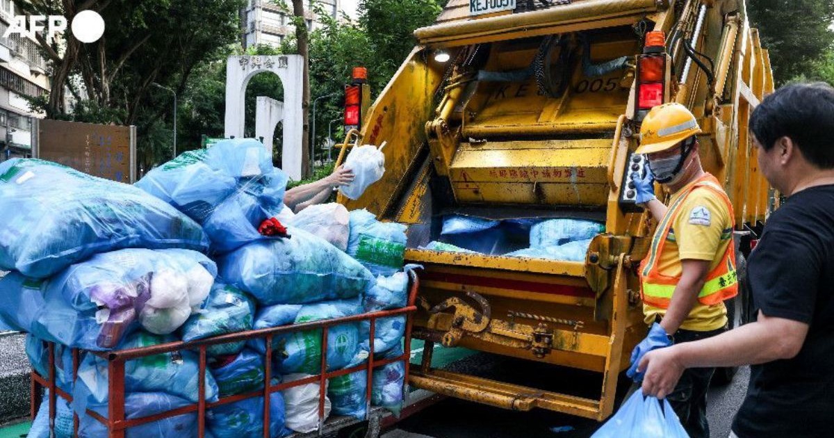 O masina de gunoi galbenă in Taipei, in timp ce ridică mai multi saci de gunoi albastri, langa masina un lucrător cu vesta și cascheta, langa el un bărbat cu un sac de gunoi in mana