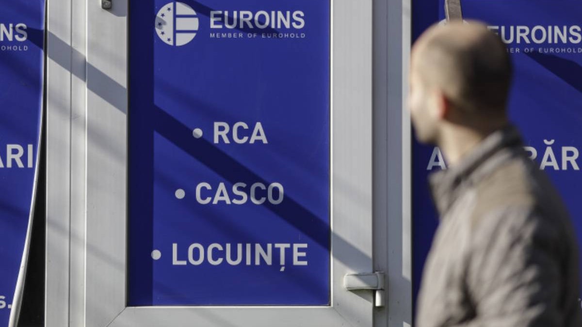 barbat care trece prin fata unui sediu euroins. pe usa sediului este lipit un autocolant cu euroins