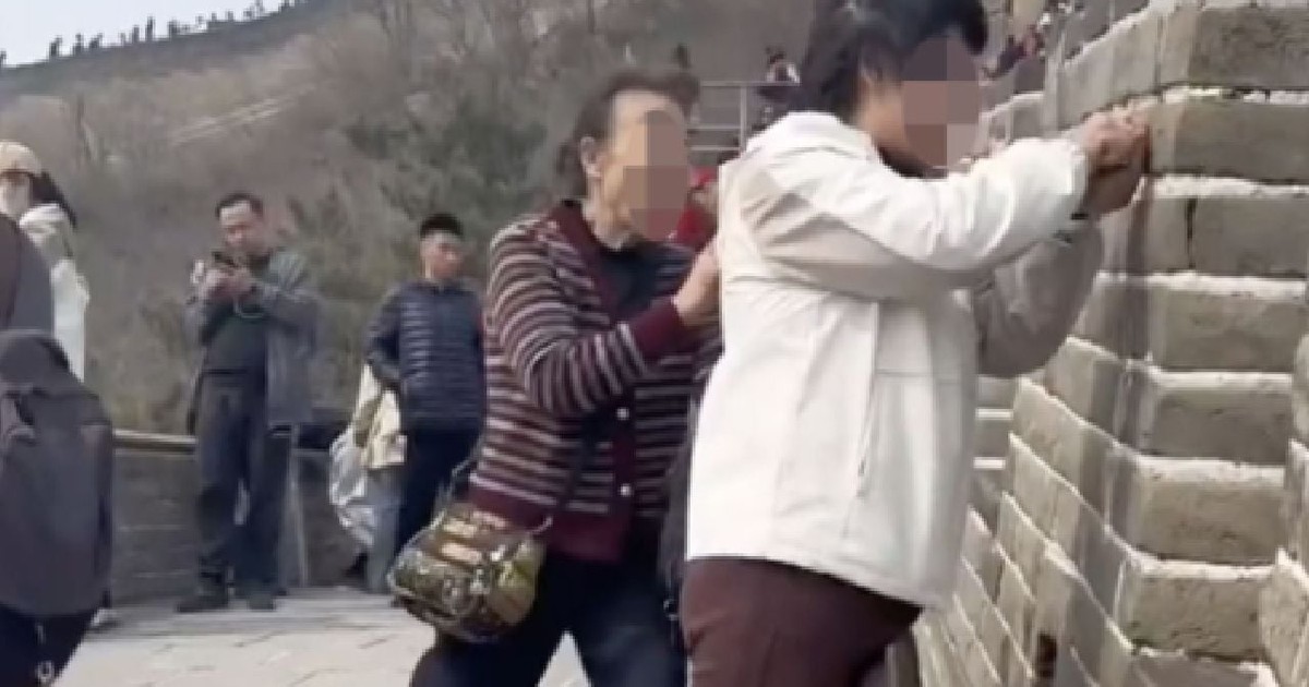 Două femei, una îmbrăcată cu o bluză albă, alta cu o geacă mov, lângă Marele Zid al Chinei