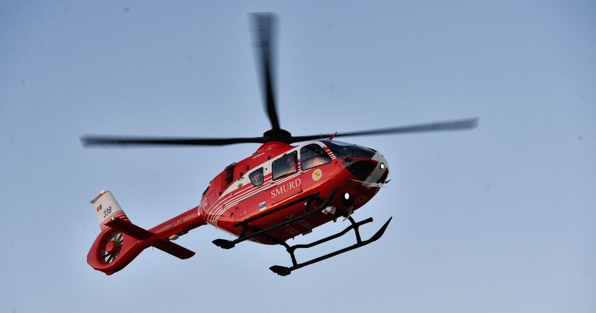 Elicopter SMURD, de culoare roșie, aflat în zbor, cu cerul albastru pe fundal