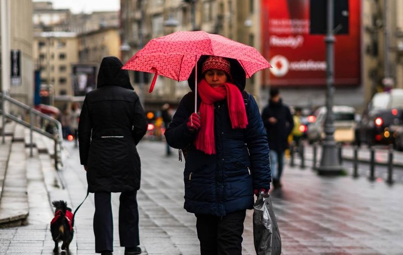 Femeie cu umbrelă plimbându-se într-o zi ploioasă pe bulevardul principal al orașului București, România