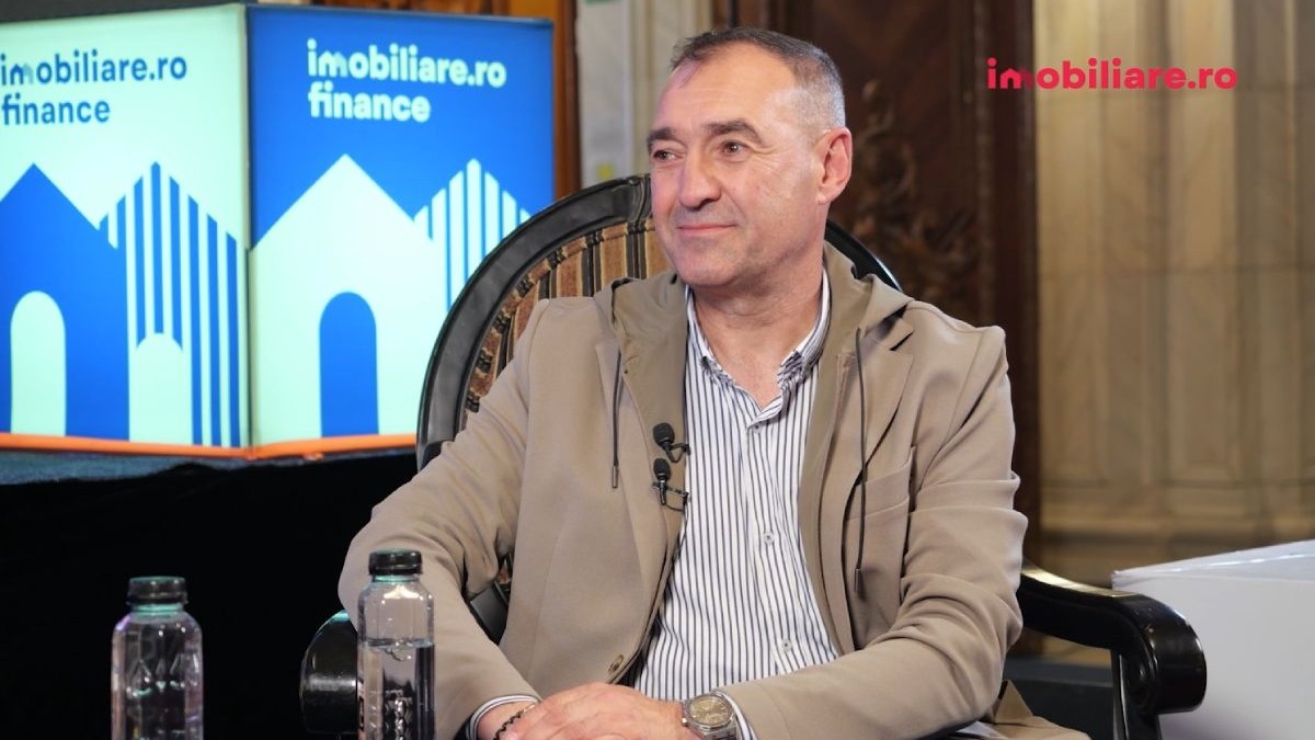Cătălin Apetri, CEO al Horizon City, în timp ce stă pe fotoliu, îmbrăcat cu o cămașă albastră cu pătrățele și o geacă scurtă de culoare crem, iar pe fundal se vede logo-ul Imobiliare.ro