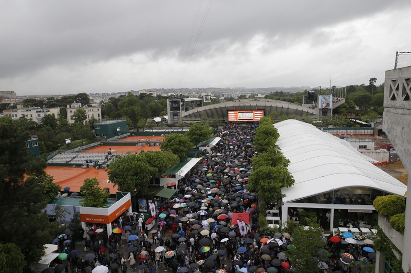 epa05323136 People walking in the rain as the first round matches are interrupted at the French Open tennis tournament at Roland Garros in Paris, France, 22 May 2016. EPA/ROBERT GHEMENT