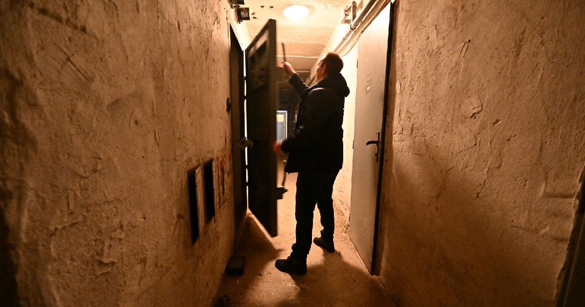În această fotografie, o persoană stă într-un coridor îngust, slab iluminat, lângă o ușă deschisă.