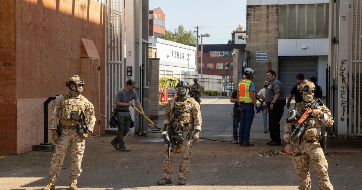 Polițiști și agenți ICE păzesc exteriorul centrului de detenție ICE, cu reprezentanța Tesla în fundal, în timp ce muncitorii acoperă toate ferestrele și intrările în centrul din Portland, Oregon, pe 16 iunie.