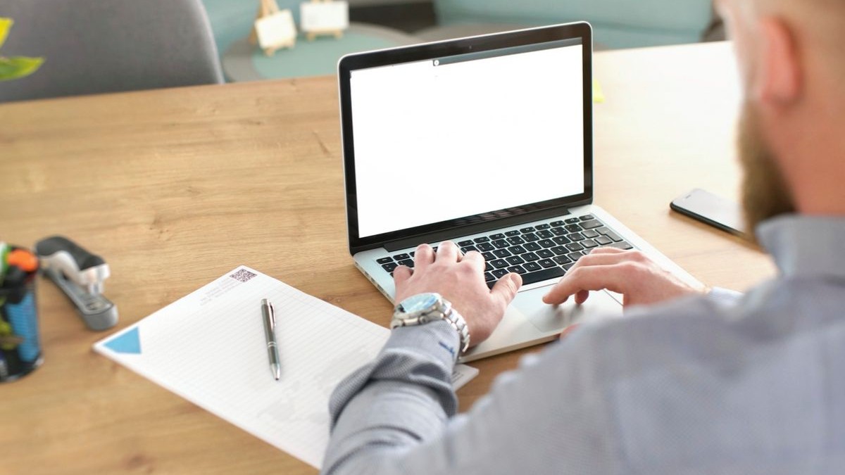 Bărbat anonim, neclar din spate, lucrând la laptop în birou, cu notebook, markere și calendar la birou, vedere din spate, detaliu pe mâini peste tastatură
