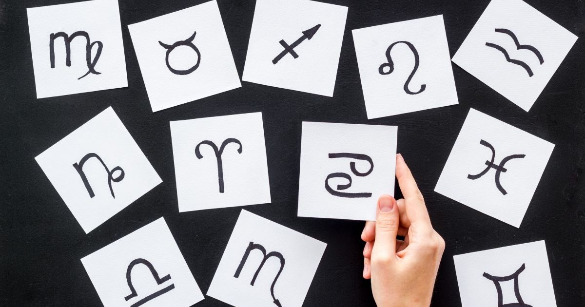 Foi de hârtie A4 cu semnele zodiacale, pe o masă de culoare neagră și o mână care ține una dintre hârtii pe care apare zodia Pești