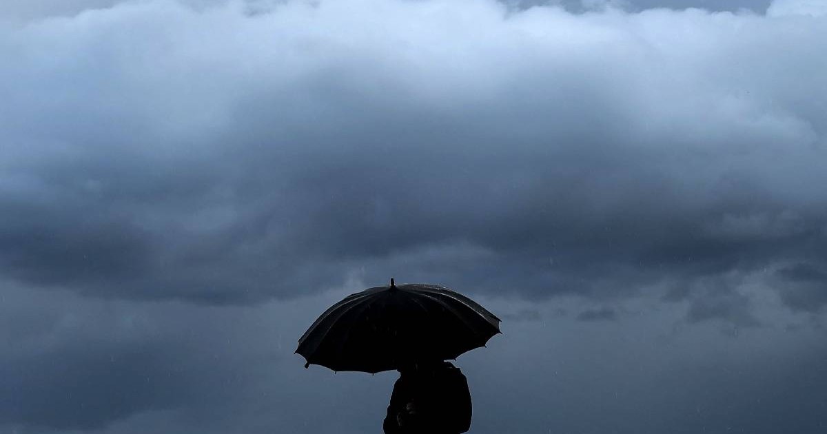o persoană stă sub umbrelă și pe fundal se vede un nor pufos de ploaie