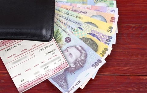 Mai multe bancnote românești ies dintr-un portofel al cărui colț negru se vede pe o masă, iar deasupra banilor este un cupon de pensie