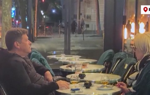O imagine cu un cuplu care savurează o băutură la o terasă din Paris, lângă Arcul de Triumf, în timpul protestelor violente, a devenit virală. Sursă foto: Captură video/ Facebook /CBS News.