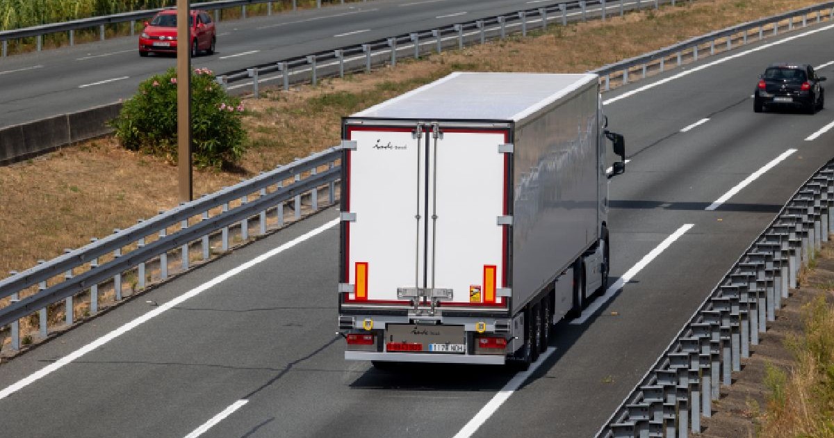 Fotografie cu un camion alb pe o autostradă cu mai multe benzi, cu parapete de protecție, o mașină neagră în fața și una roșie pe sensul opus.