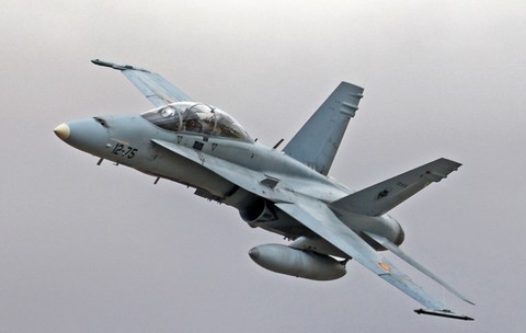 Un avion de luptă F/A-18 Hornet surprins în zbor în timp ce efectuează o manevră de urcare pe un cer înnorat.   