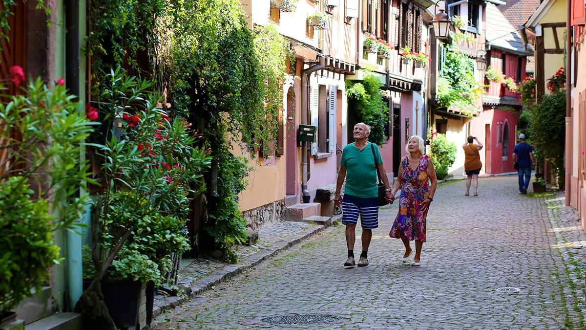 Cuplu de seniori activi care călătoresc în Franța. Persoane în vârstă vizitând regiunea Alsacia, plimbându-se pe străzile orașului Kaysersberg. Bărbat și femeie bucurându-se de orașele, satele și peisajul rural francez