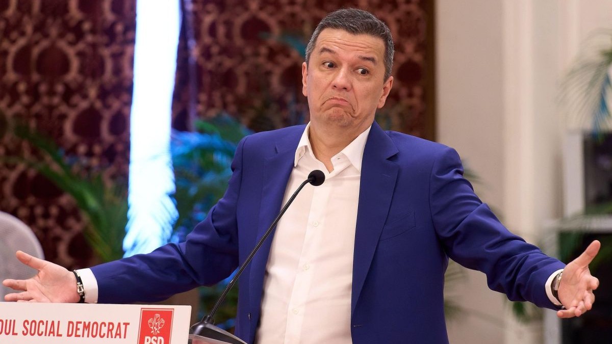 Sorin Grindeanu, îmbrăcat într-un sacou albastru și cămașă albă, când ridică ambele mâini și umerii, la pupitrul cu sigla PSD, într-o conferință de presă pe 31 iulie 2026
