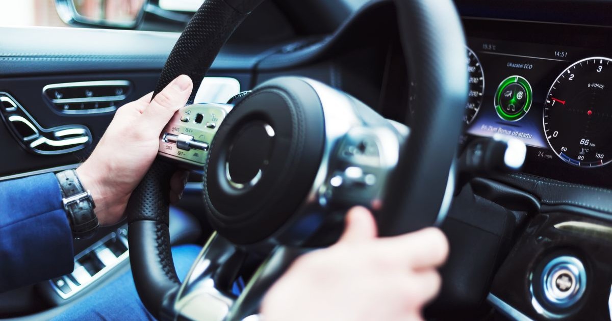 Un bărbat se află la volan și conduce o mașină. Se văd ambele mâini ale șoferului și bordul mașinii