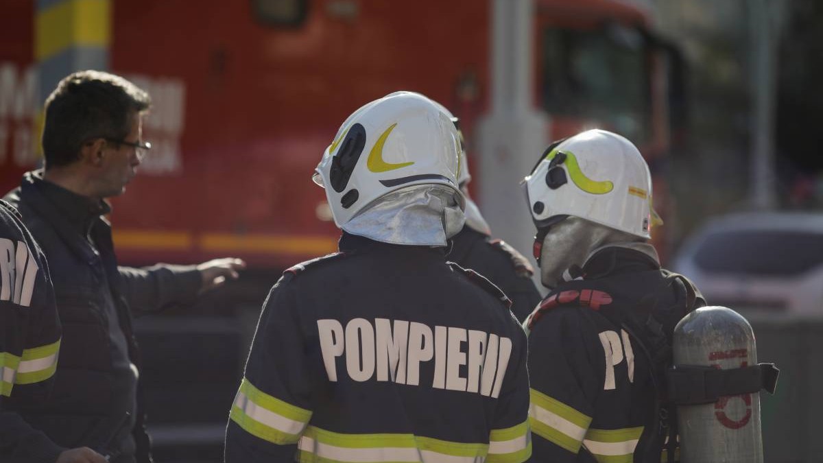 Mai mulți pompieri lângă autospeciala de stingere în timp ce așteaptă noi indicații
