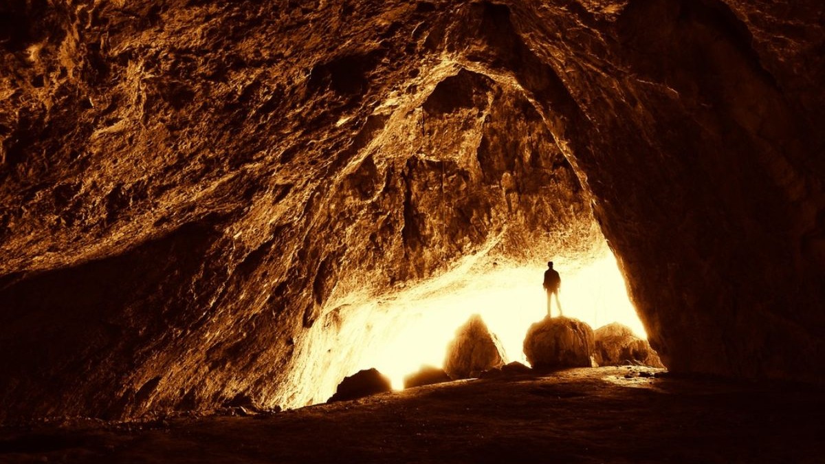 Silueta unui bărbat la intrarea unei pesteri, fotografie facuta din interior,silueta se vede inundată de lumină