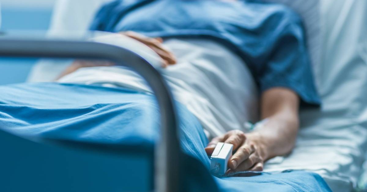 Un pacient cu asigurare de sănătate care stă pe patul de spital, este învelit și are un pulsoximetru montat