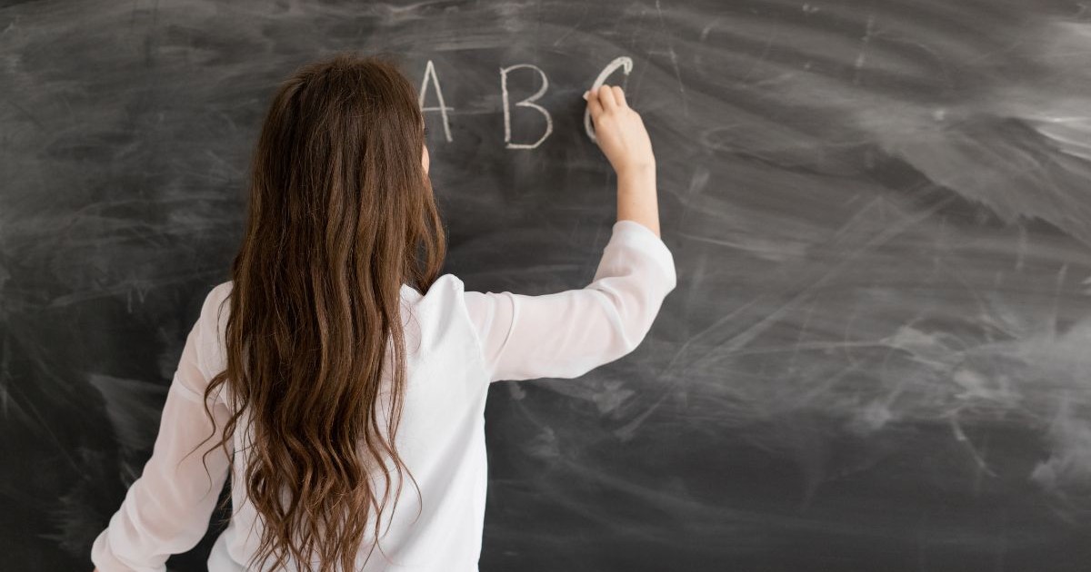 profesoară care scrie litere pe o tablă cu cretă