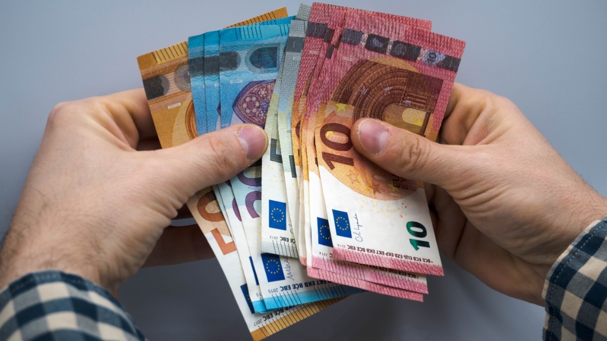 O persoană care ține bancnote de euro în mână